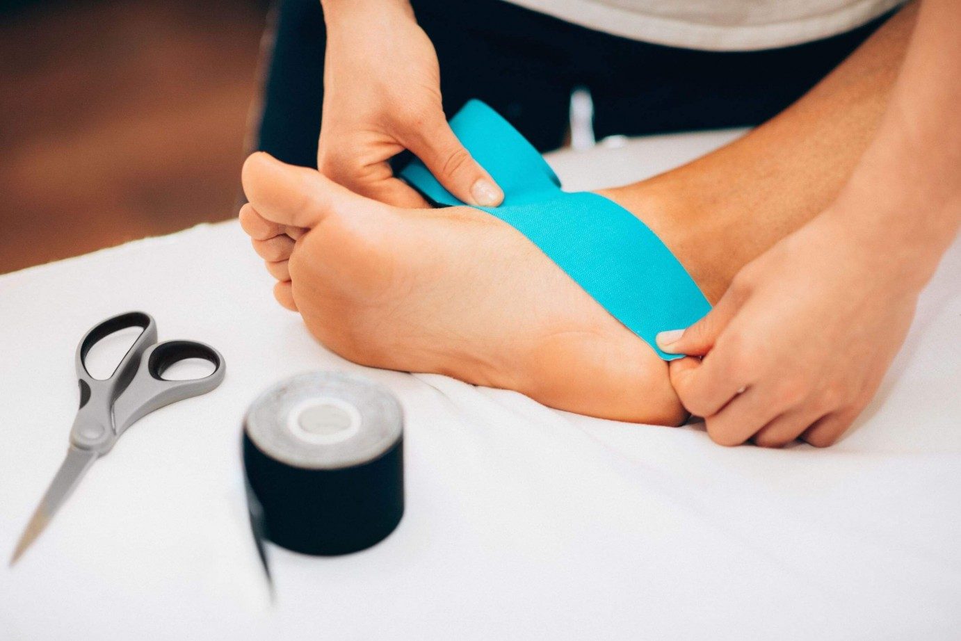 Two hands starting to strap the side of a foot with blue tape