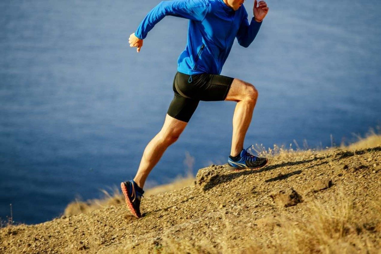 A man's legs running up a dirt hill beside the ocean