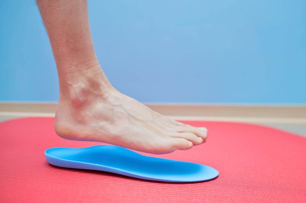 A foot hovering above a blue orthotic that is on a pink mat