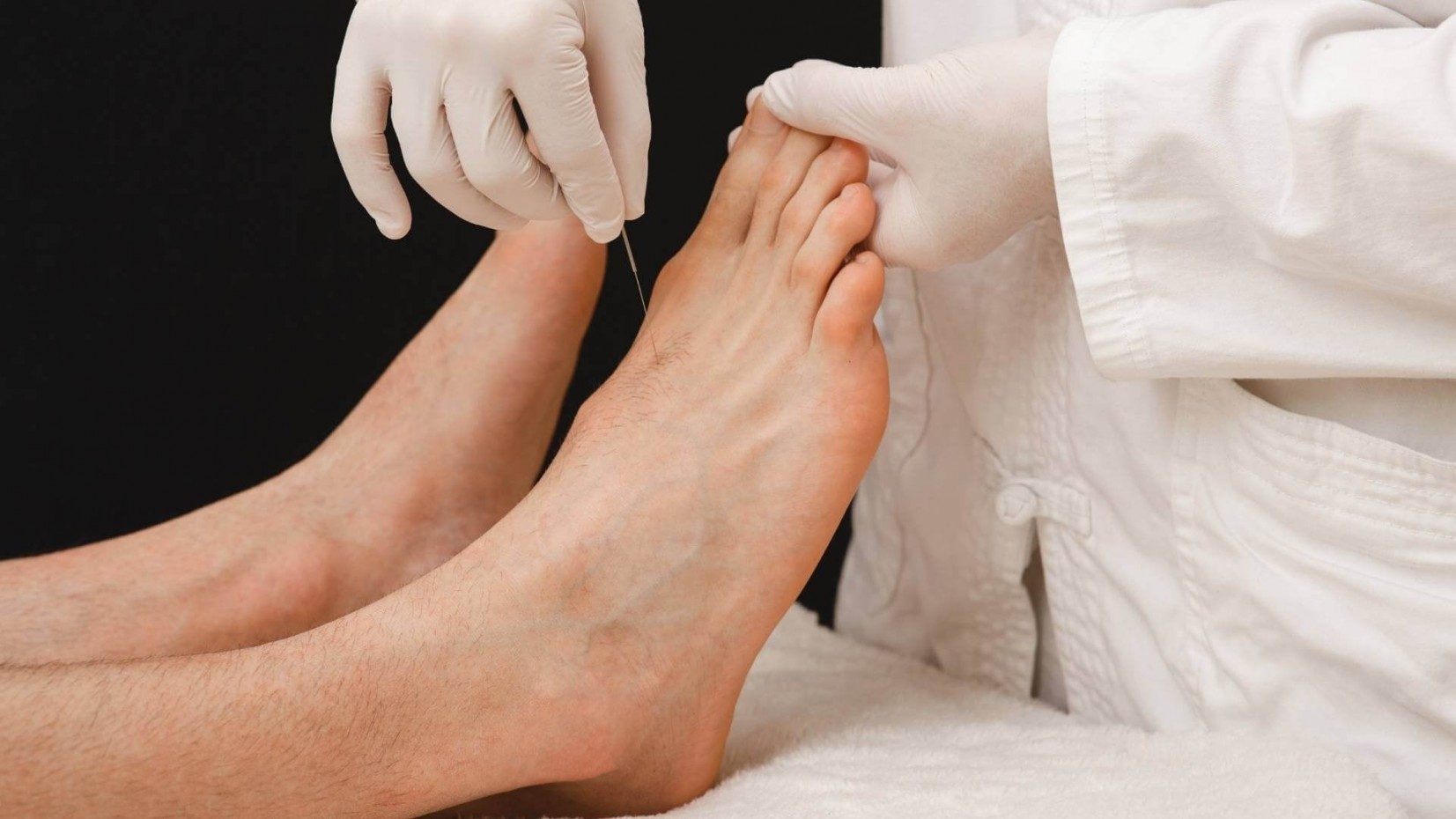 a white gloved hand sticking a thin needle into a foot
