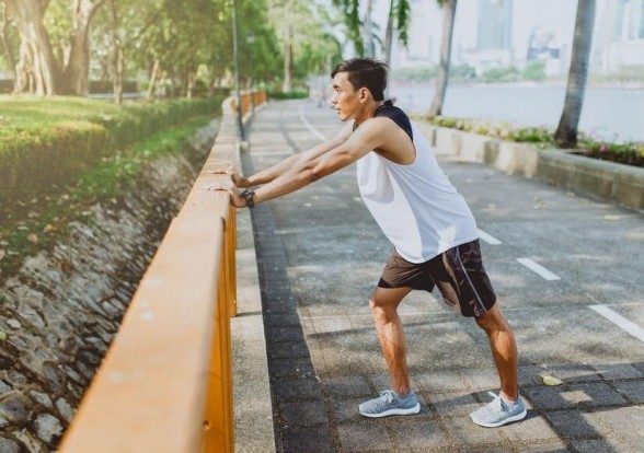 Man leaning forward on the railing with one foot forward, stretching the back leg's calf.