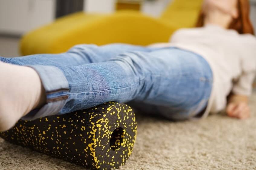 Release tension in your feet A woman in jeans lying down with her calves over a black and yellow foam roller