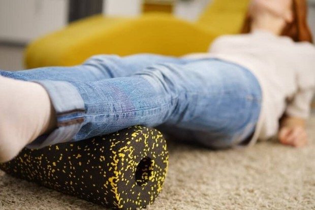 A woman in jeans lying down with her calves over a black and yellow foam roller