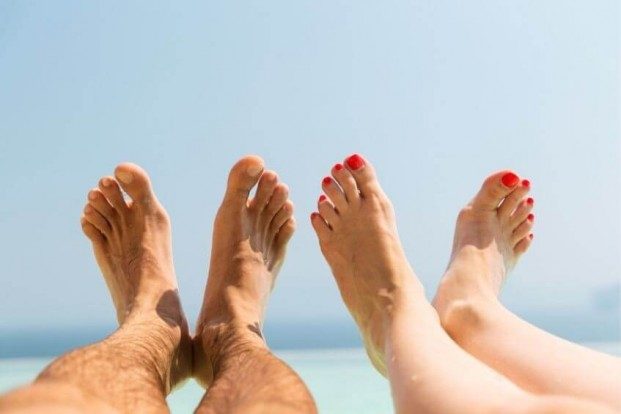 One pair of men's feet next to one pair of women's feet hovering in the air above a blue ocean