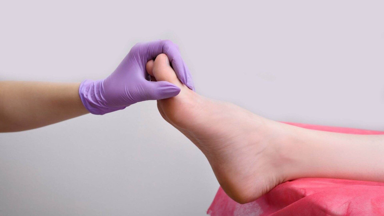 A side view of a hand in a purple glove holding a foot 