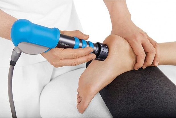A physician holding a person foot and applying the shockwave machine handle to the bottom of their foot