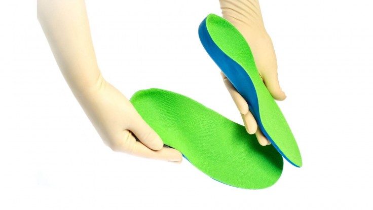 Two hands holding two green custom foot orthotics