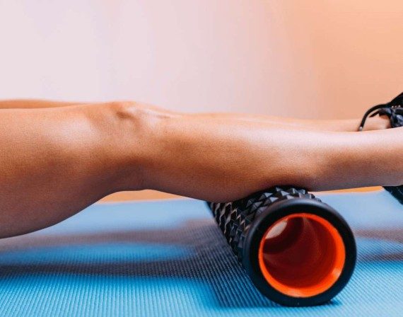 Fit young woman stretching and rolling her calves with a foam roller