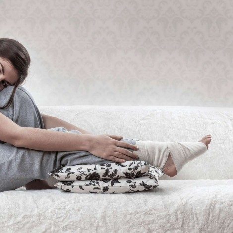 A girl with an injured foot has it elevated on a cushion to reduce swelling