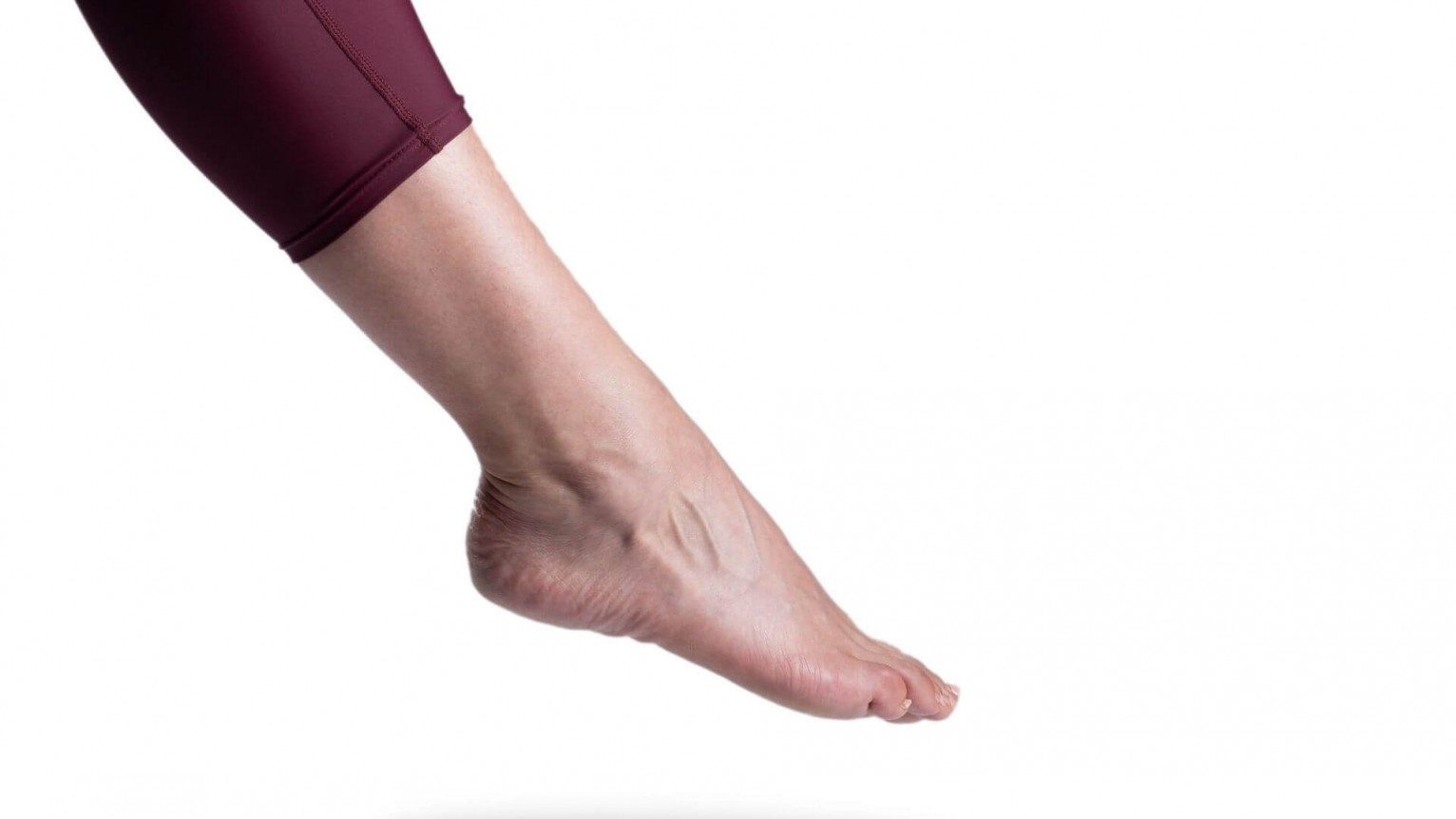 Side view of a white woman's ankle and pointing foot.  A pair of purple maroon leggings stop just above the ankle