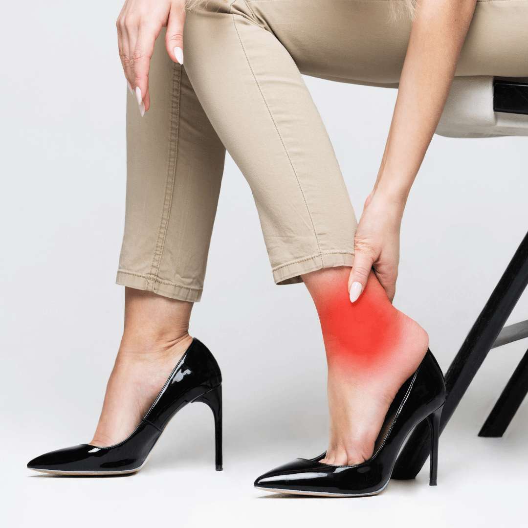 Woman in high heels sitting down holding her ankle and heel in pain