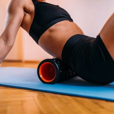 Woman's leg foam rolling her lower back on yoga mat