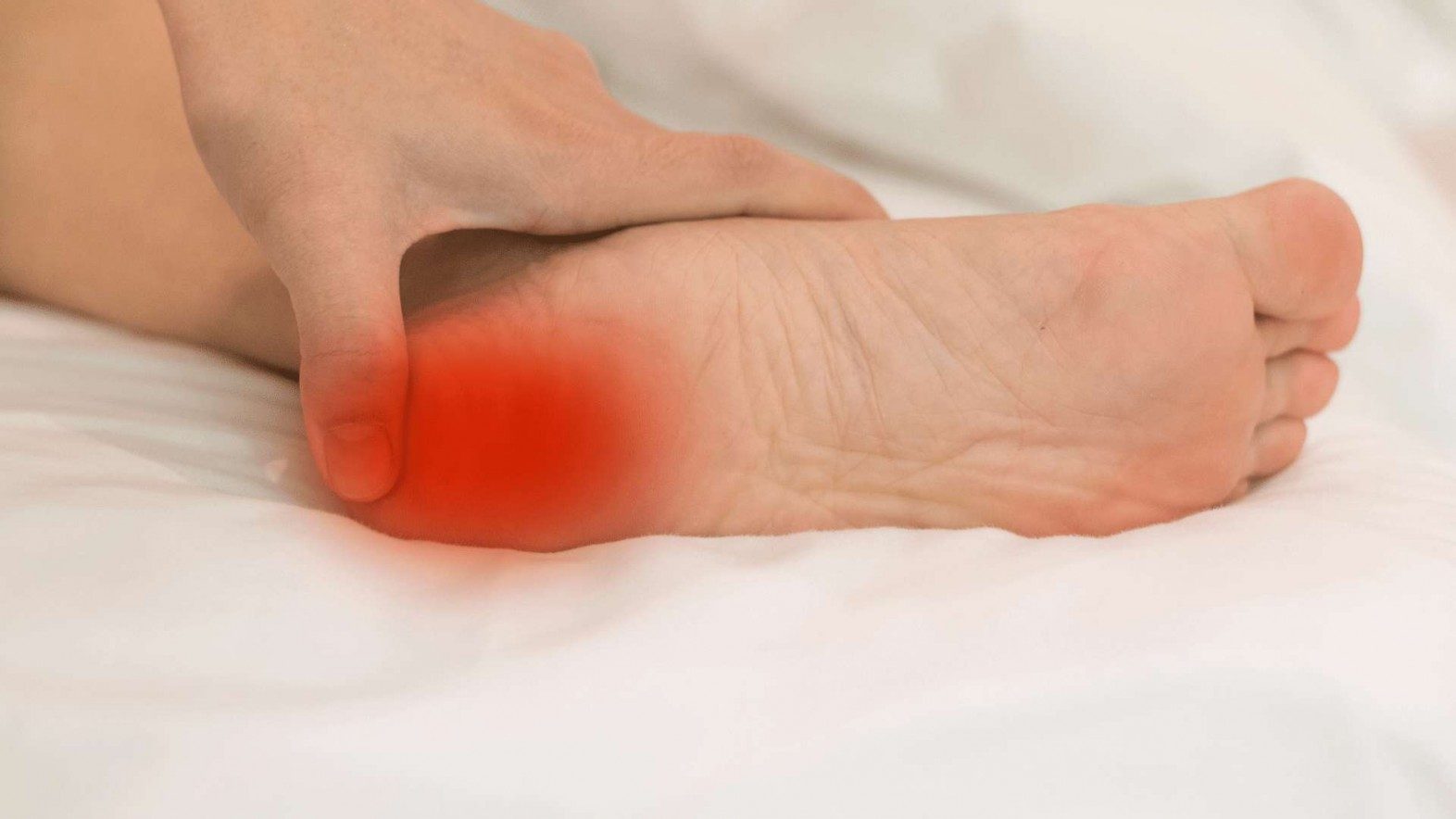A hand holding their foot in pain from plantar fasciitis, with a red pain locator on the heel