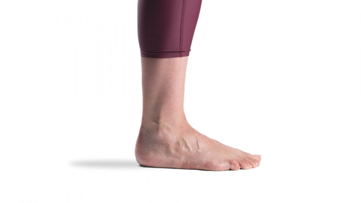 Side view of a white woman's ankle and foot.  A pair of purple maroon leggings stop just above the ankle